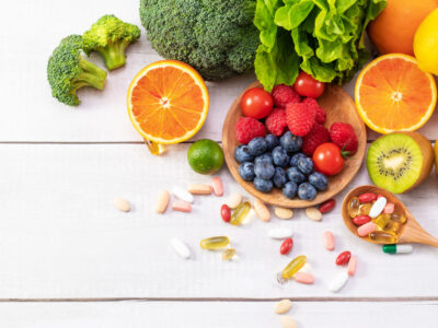 A top view of fresh fruits and vegetables with different medicine on a wooden spoon